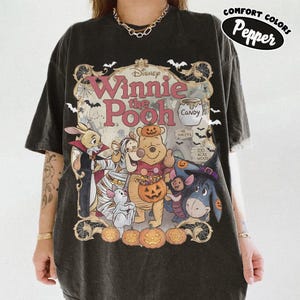 May include: A charcoal gray t-shirt featuring a graphic of Winnie the Pooh characters dressed in Halloween costumes. The design includes Pooh, Piglet, Tigger, Eeyore, and Rabbit surrounded by pumpkins, bats, and spiderwebs with the text Winnie the Pooh.
