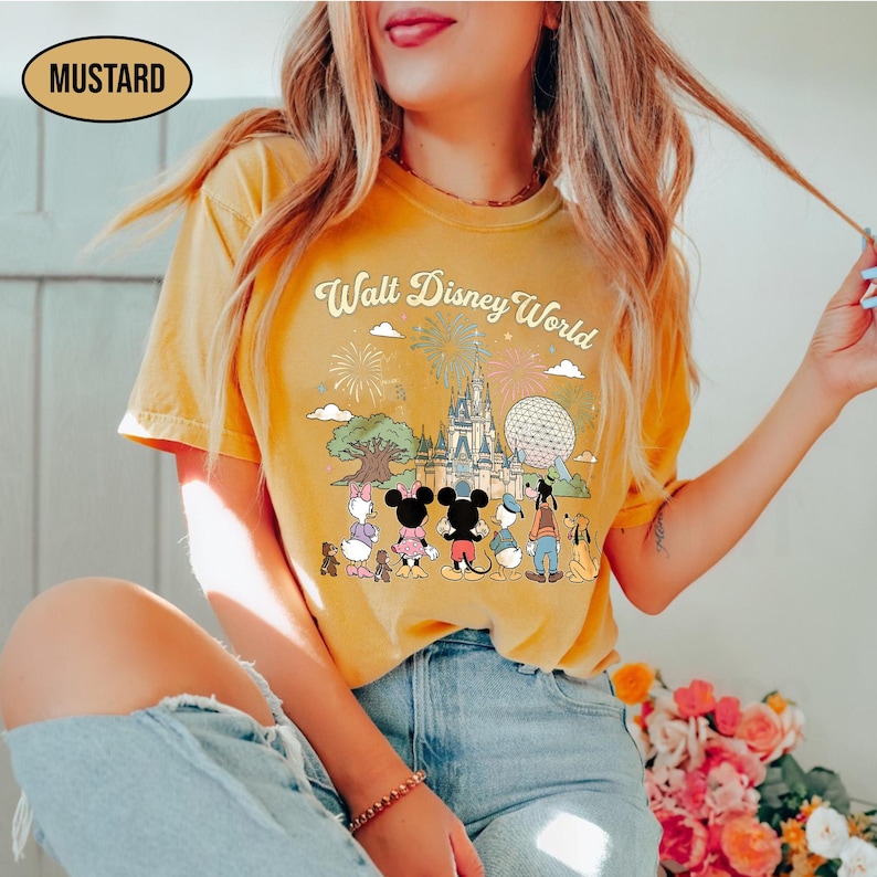 May include: Mustard-coloured t-shirt with a graphic of Disney characters in front of Cinderella's castle and the text "Walt Disney World". The shirt has a retro design with fireworks and clouds.