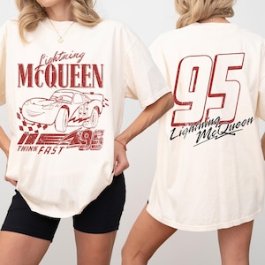 Puede incluir: Camiseta color crema con un gr&aacute;fico de Lightning McQueen en rojo. El dise&ntilde;o frontal incluye el coche, el texto "Lightning McQueen", "95" y "Think Fast". La parte trasera muestra un gran "95" y "Lightning McQueen" en rojo y negro.