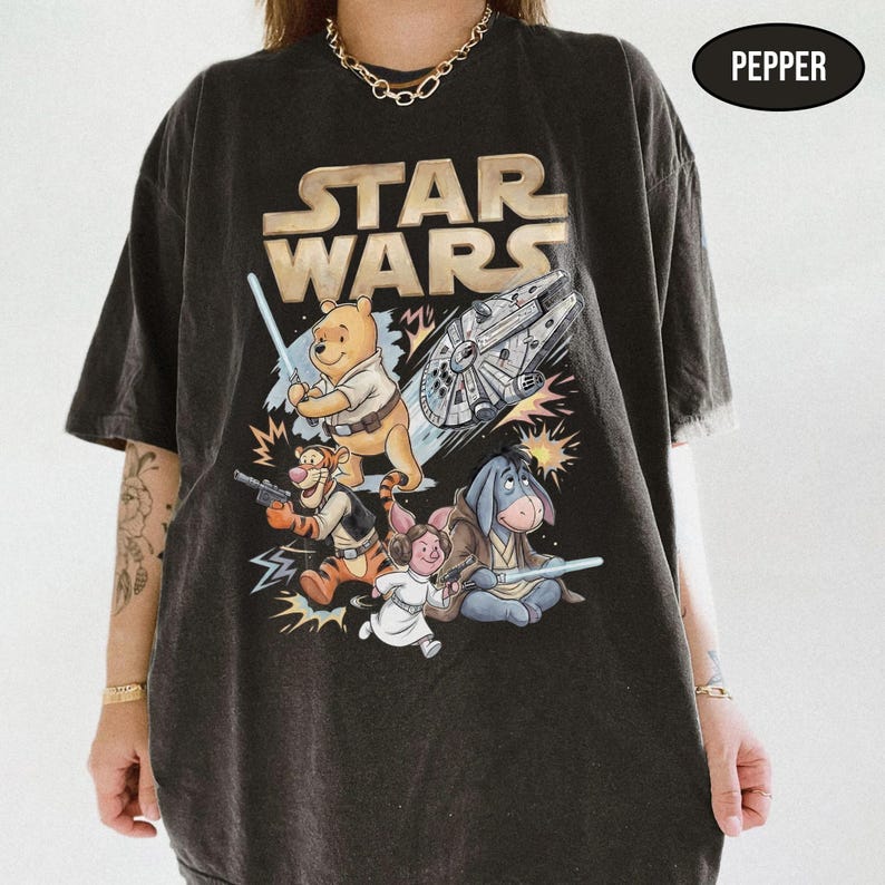 Puede incluir: Camiseta gris oscuro con un dise&ntilde;o que combina Star Wars y Winnie the Pooh. El dise&ntilde;o incluye el logo de Star Wars, un Halc&oacute;n Milenario y personajes como Winnie the Pooh, Tigger, &Iacute;gor y la Princesa Leia con sables de luz y bl&aacute;sters.