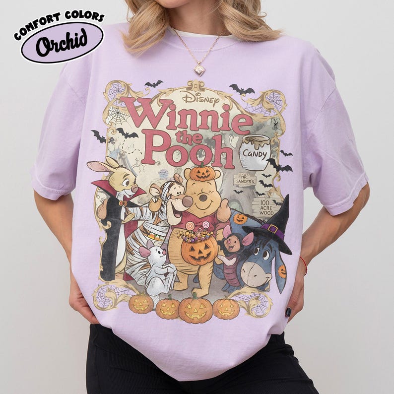 May include: A light purple t-shirt featuring a graphic of Winnie the Pooh characters dressed in Halloween costumes. The design includes Pooh, Piglet, Tigger, Eeyore, and Rabbit surrounded by pumpkins, bats, and spiderwebs with the text Winnie the Pooh.