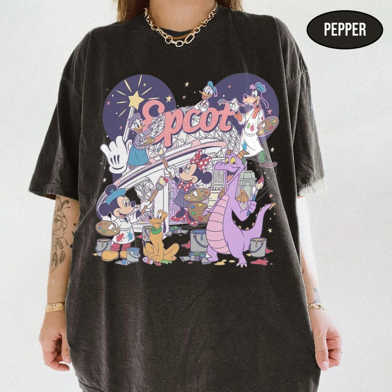 May include: Dark gray t-shirt featuring a colorful graphic of Disney characters painting the word "Epcot". The design includes Mickey Mouse, Minnie Mouse, Donald Duck, Pluto, and Figment. The shirt has a vintage, distressed look.