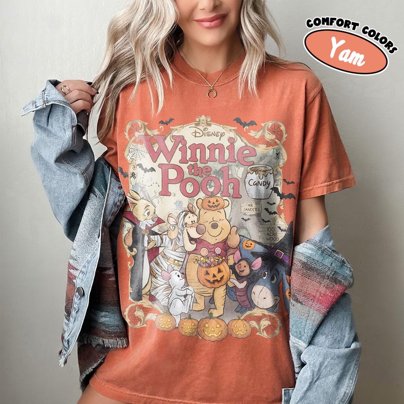 May include: A burnt orange short-sleeve t-shirt featuring a graphic of Winnie the Pooh and friends in Halloween costumes. The print includes the text Disney Winnie the Pooh, Candy, Mr. Sanders, and 100 Acre Wood, with pumpkins and bats.