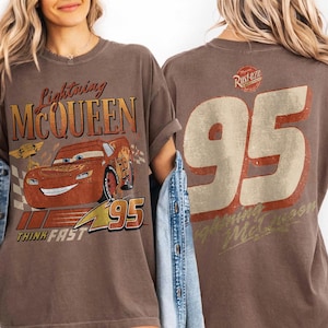 May include: Brown t-shirt featuring Lightning McQueen from the Cars film. The front graphic includes the character's image, the text "Lightning McQueen", and the number "95". The back displays a large "95" and the text "Lightning McQueen".