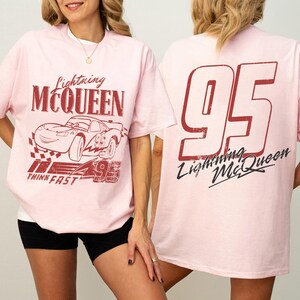 Puede incluir: Camiseta rosa claro con gr&aacute;ficos de Rayo McQueen. La parte delantera muestra el nombre y la imagen del personaje, junto con el n&uacute;mero 95. La parte trasera de la camiseta tiene un gran n&uacute;mero 95 y el logotipo de Rayo McQueen. Prenda casual.