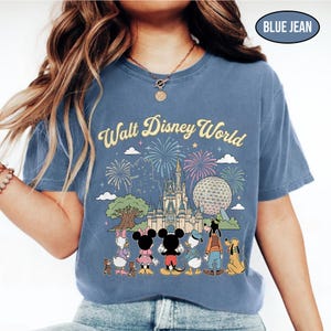 May include: Blue jean-coloured t-shirt with a Walt Disney World graphic. The design shows Cinderella's castle, Spaceship Earth, fireworks, and Disney characters such as Mickey and Minnie Mouse. The text "Walt Disney World" is arched across the top.