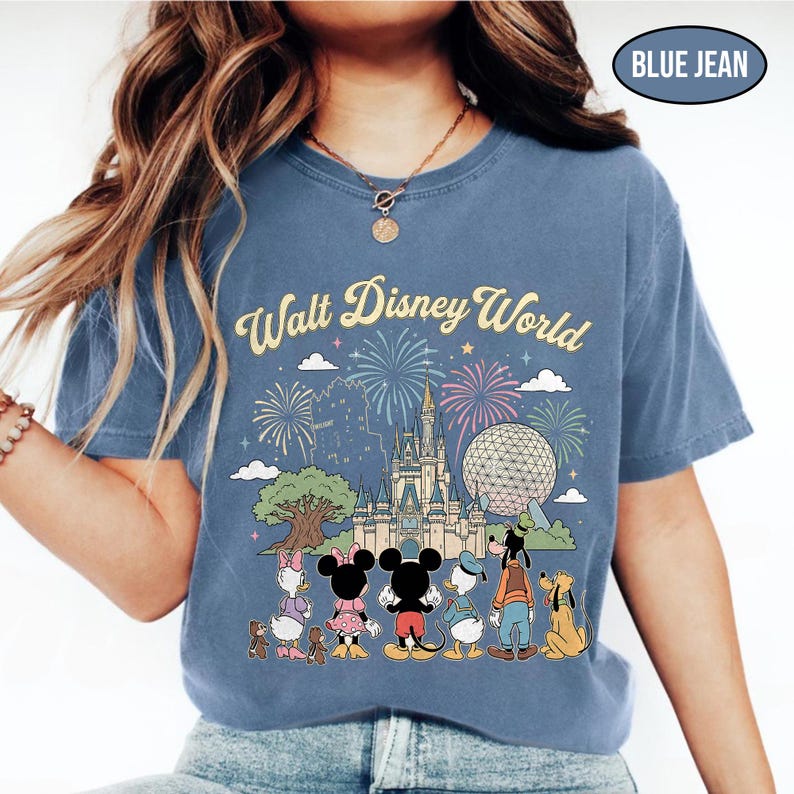 May include: Blue jean-coloured t-shirt with a Walt Disney World graphic. The design shows Cinderella's castle, Spaceship Earth, fireworks, and Disney characters such as Mickey and Minnie Mouse. The text "Walt Disney World" is arched across the top.