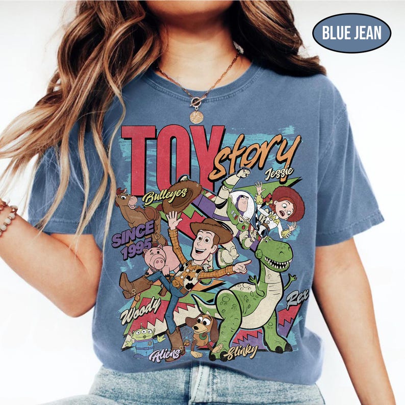 Puede incluir: Camiseta azul vaquero con un gr&aacute;fico de personajes de Toy Story. El dise&ntilde;o incluye a Woody, Buzz Lightyear, Jessie, Rex y otros personajes de la pel&iacute;cula. El texto "TOY STORY" se muestra de forma destacada, junto con "SINCE 1995".