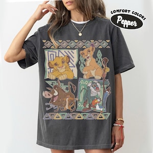 May include: A charcoal gray short-sleeve t-shirt featuring a graphic print of characters from The Lion King, including Simba, Nala, Pumbaa, Timon, Rafiki, and Zazu, arranged in four panels with geometric borders and the text Comfort Colors Pepper.