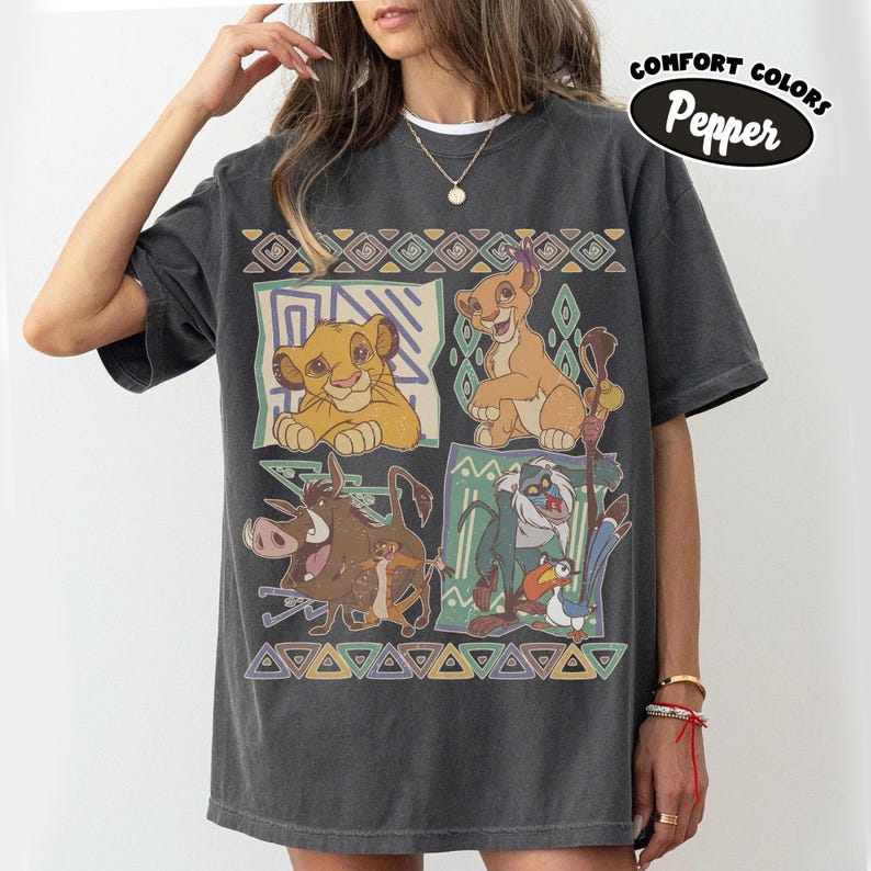 May include: A charcoal gray short-sleeve t-shirt featuring a graphic print of characters from The Lion King, including Simba, Nala, Pumbaa, Timon, Rafiki, and Zazu, arranged in four panels with geometric borders and the text Comfort Colors Pepper.