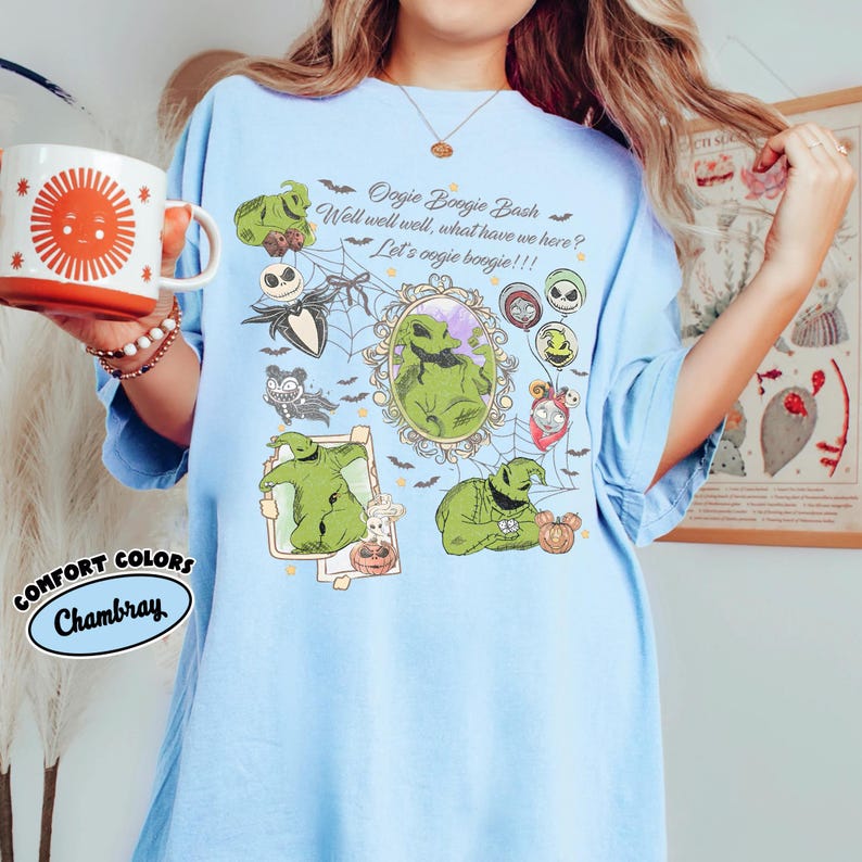 May include: Light blue t-shirt with a graphic featuring Oogie Boogie from The Nightmare Before Christmas. The design includes the text "Oogie Boogie Bash" and "Well well well, what have we here? Let's oogie boogie!!!". The shirt is labeled "Comfort Colors Chambray".