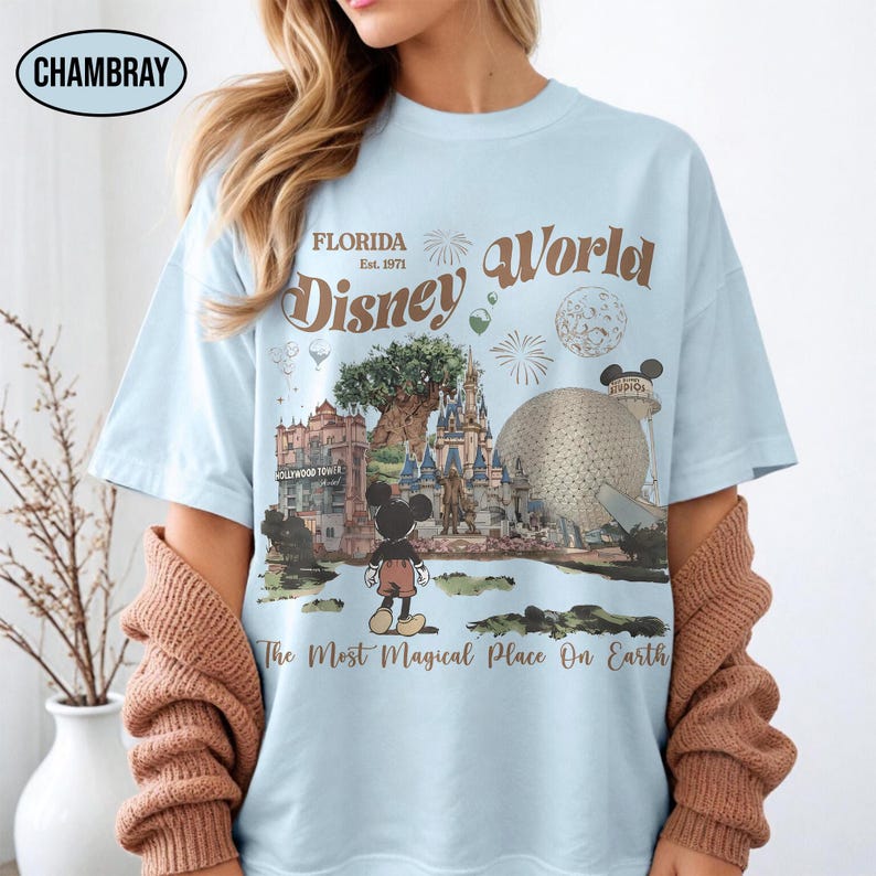 Puede incluir: Camiseta azul claro con un dise&ntilde;o de Disney World. El gr&aacute;fico incluye el texto "Florida Disney World Est. 1971" con im&aacute;genes de los monumentos del parque y Mickey Mouse. La camiseta tambi&eacute;n tiene la frase "The Most Magical Place On Earth".