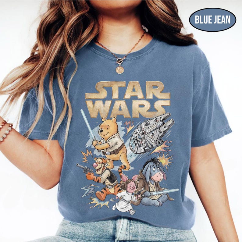 Puede incluir: Camiseta azul vaquero con un gr&aacute;fico de Star Wars con personajes de Winnie the Pooh. El dise&ntilde;o incluye a Winnie the Pooh con un sable de luz, Tigger con un blaster y otros personajes con el Halc&oacute;n Milenario.