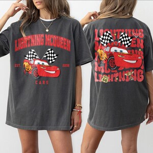 Peut inclure: T-shirt gris fonc&eacute; avec Lightning McQueen du film Cars. Le devant affiche le texte "LIGHTNING MCQUEEN" et "CARS" avec une voiture de course et des drapeaux &agrave; damier. Le dos du t-shirt reprend le motif.
