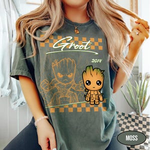 Puede incluir: Camiseta verde musgo con un gr&aacute;fico de Groot. El dise&ntilde;o incluye la palabra "Groot" sobre una imagen de dibujos animados de Groot, con el a&ntilde;o "2014" debajo. La camiseta tiene un patr&oacute;n de cuadros y un aspecto desgastado.