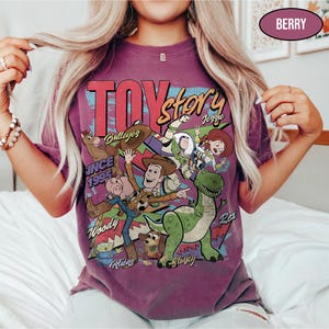 Puede incluir: Camiseta color bayas con un gr&aacute;fico de Toy Story que presenta a Woody, Buzz Lightyear y Rex. El dise&ntilde;o incluye el texto "TOY STORY" y "SINCE 1995". La camiseta tiene un aspecto vintage y desgastado.