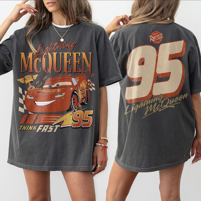 May include: Charcoal grey Lightning McQueen t-shirt with a large graphic of the character and the number 95. The front of the shirt displays the text "Lightning McQueen" and "Think Fast". The back of the shirt has the number 95 and "Lightning McQueen".