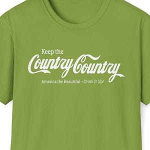 May include: A lime green t-shirt with the phrase "Keep the Country Country" in white script. Below the script, the text reads "America the Beautiful—Drink It Up!" The shirt has a crew neck and short sleeves.