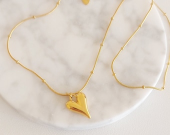 May include: A gold chain necklace with a large, heart-shaped pendant. The chain has small, round beads.