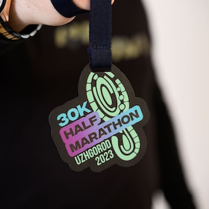 May include: A black and green medal with the text "30K HALF MARATHON UZHGOROD 2023" and a stylized footprint design.