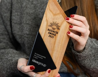 May include: A wooden award plaque with a black plaque inset. The wooden plaque has a sun graphic and the text "BUSINESS AWARD 2023". The black plaque has the text "The fastest growing line of business in 2023 ideagroup".