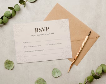 Pode incluir: Um cartão RSVP com detalhes florais, um envelope castanho e uma caneta de madeira. O cartão diz "RSVP" e "Por favor, responda até 15 de maio". Inclui espaços para nomes, aceitação, recusa e necessidades dietéticas. Folhas de eucalipto são visíveis.