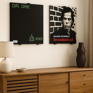 May include: Two framed album art prints on a wall. One is black with "DR. DRE" and "2001" in green, plus a green cannabis leaf. The other features Nick Cave & The Bad Seeds' album "the boatman's call".