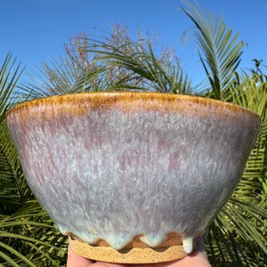 May include: A large, handmade ceramic bowl with a light blue glaze and a brown rim. The bowl has a unique, drippy glaze effect and a wavy edge.