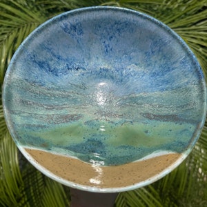 May include: A ceramic bowl with a blue, green, and brown glaze. The glaze resembles a beach scene with a sandy beach, blue water, and green grass.