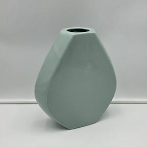 May include: A pale mint green ceramic vase with a smooth, glossy finish. The vase features a distinct geometric, teardrop-like shape with flat, angled sides that taper toward a small, circular opening at the top, creating a clean, modern silhouette.