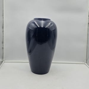 May include: A smooth, dark navy blue vase with a rounded, bulbous body that tapers toward a narrow, circular opening at the top. The surface of the vase has a glossy, reflective finish that catches the light, highlighting its curved silhouette.