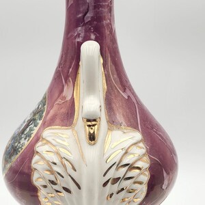 May include: A pink and white ceramic table lamp with a gold trim and a white swan design. The lamp has a brown base with a decorative design.