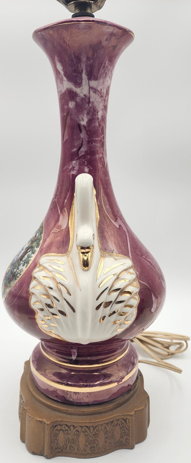 May include: A pink and white ceramic table lamp with a gold trim and a white swan design. The lamp has a brown base with a decorative design.