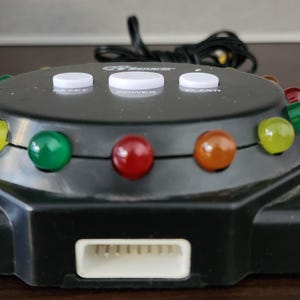 May include: A black plastic game with a circular base and a ring of colored lights. The lights are red, yellow, and green. There are three white buttons on the top of the game labeled "Reset", "Power", and "Start".