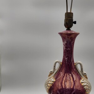 May include: A vintage ceramic table lamp with a pink and white marbled base. The base features two white swan handles and gold accents. The lamp has a brown wooden base with gold accents.