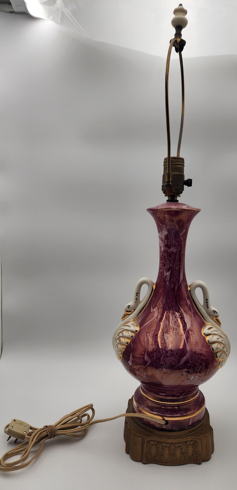 May include: A vintage ceramic table lamp with a pink and white marbled base. The base features two white swan handles and gold accents. The lamp has a brown wooden base with gold accents.
