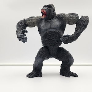 May include: A black gorilla action figure with a large mouth and sharp teeth. The figure is posed in a standing position with its arms raised and its fists clenched.