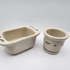 Puede incluir: Dos piezas de cerámica blanquecina con temática navideña. Una es una fuente rectangular para pan, y la otra es un pequeño recipiente redondo. Ambas tienen un diseño de acebo verde y rojo. La fuente mide unos 18 cm de largo.