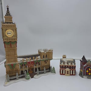 May include: A collection of miniature ceramic buildings, including a detailed replica of Big Ben, a church, and other structures. The buildings are painted with festive colors and adorned with decorative elements, suggesting a holiday theme.