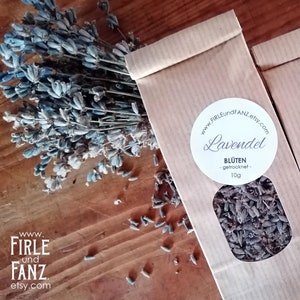 Può includere: Due sacchetti di carta marrone con etichette bianche che recitano "Lavendel" e "BLÜTEN -getrocknet- 10g". I sacchetti contengono fiori di lavanda secchi.