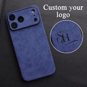 Peut inclure: Coque de téléphone bleu marine avec une texture semblable à du daim. L'étui a une découpe pour l'appareil photo et le texte "Custom your logo" est visible. Un patch circulaire affiche un logo avec le texte "SAMIRA HADID" et les initiales "SH".