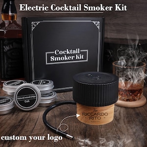 Op de afbeelding: Een elektrische cocktailrokerkit met een zwarte roker, houten basis en een flexibele slang. De kit bevat kleine blikken met houtsnippers en een zwarte doos met het opschrift "Cocktail Smoker Kit". De tekst "custom your logo" staat onderaan.