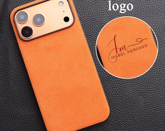 Può includere: Custodia per telefono arancione con cornice della fotocamera dorata. La custodia ha una consistenza simile alla pelle scamosciata e il testo "Custom your logo" è visibile. Un inserto circolare mostra un logo con la scritta "ISABEL MERCADO".