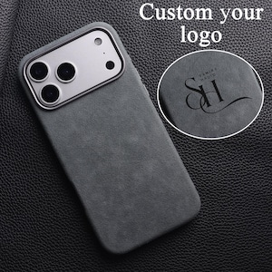 May include: A dark gray phone case with a silver camera module. The case has a textured surface and the words "Custom your logo" are at the top. A circular inset shows a logo with the text "SAMIRA HADID" and the initials "SH".