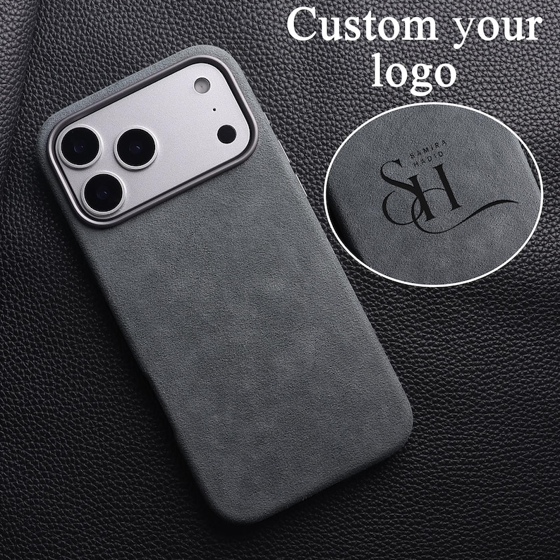 May include: A dark gray phone case with a silver camera module. The case has a textured surface and the words "Custom your logo" are at the top. A circular inset shows a logo with the text "SAMIRA HADID" and the initials "SH".