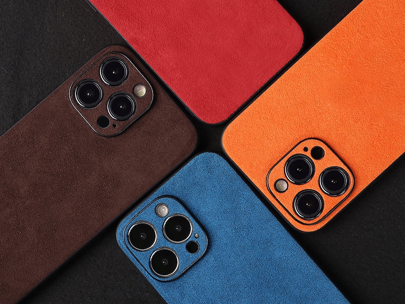 May include: Four different coloured phone cases with a suede-like texture. Each case has a camera lens cutout with three black circles.
