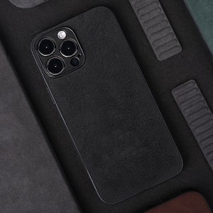 May include: A black phone case with a textured surface and a camera lens with three black circles. The case is lying on a black surface.