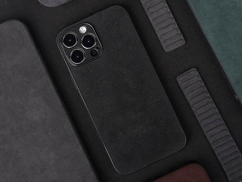 May include: A black phone case with a textured surface and a camera lens with three black circles. The case is lying on a black surface.