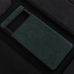 Pode incluir: Uma capa de telefone verde escura com uma moldura preta. A capa tem um acabamento texturizado, semelhante a camur&ccedil;a.