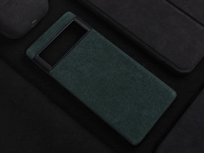 Pode incluir: Uma capa de telefone verde escura com uma moldura preta. A capa tem um acabamento texturizado, semelhante a camur&ccedil;a.